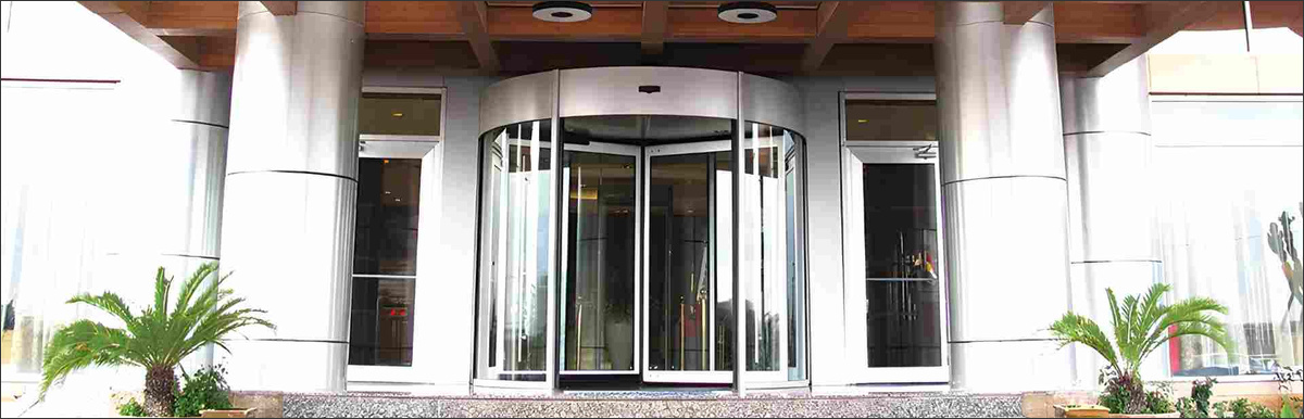 Puerta automática giratoria de Manusa en un acceso a edificio, pensada para separar el interior y el exterior climatizados