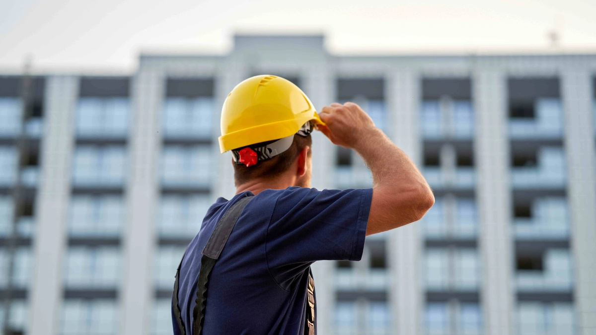 Trabajador de espaldas con casco amarillo frente a un edificio.
